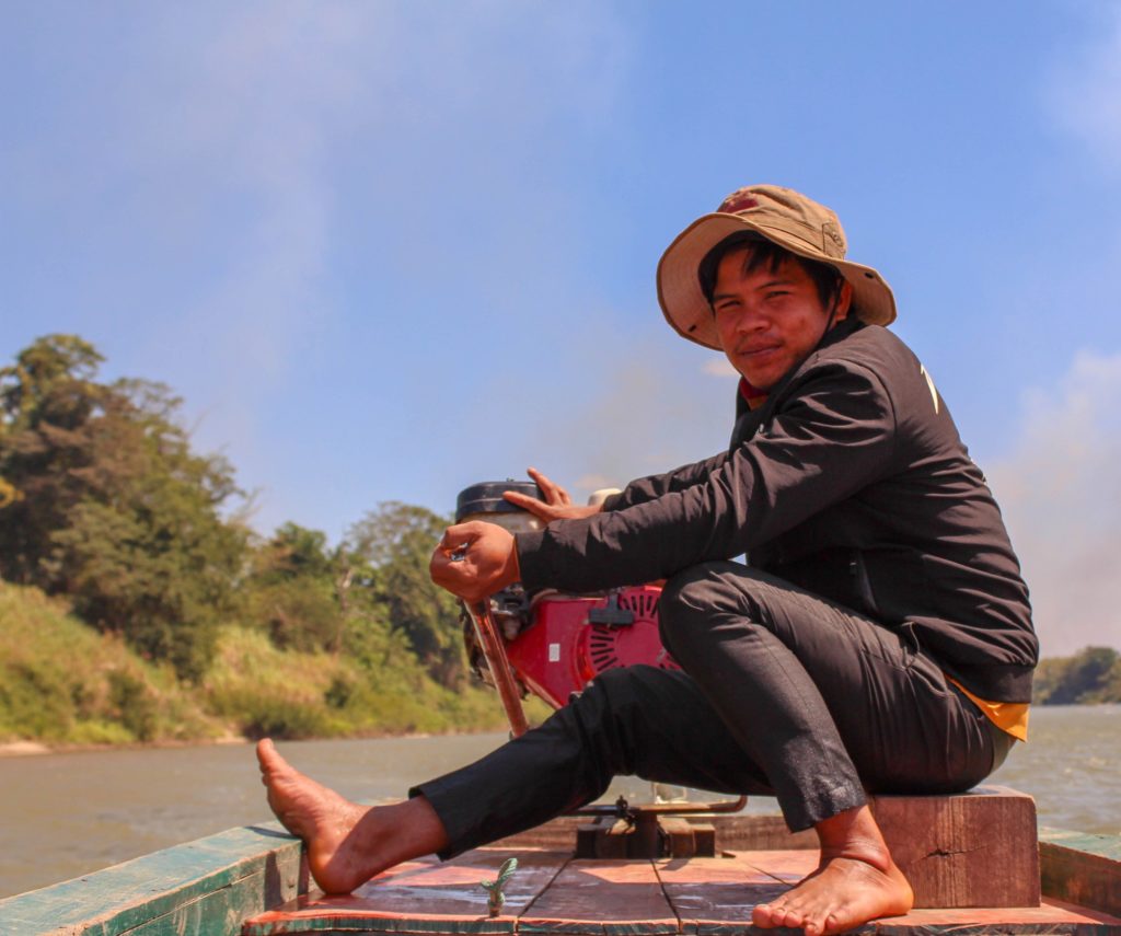 A member of our malaria outreach team sits on the bow of a boat next to the motor