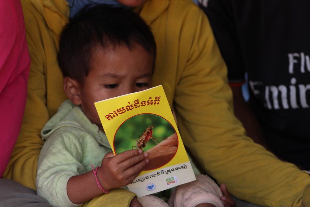 A small boy inspects a pamphlet about malaria as he sits on his mother's lap