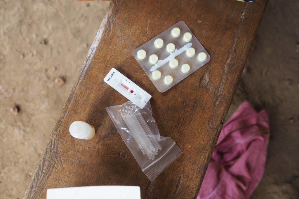 A malaria diagnostic kit and malaria drugs lie out on a bench.