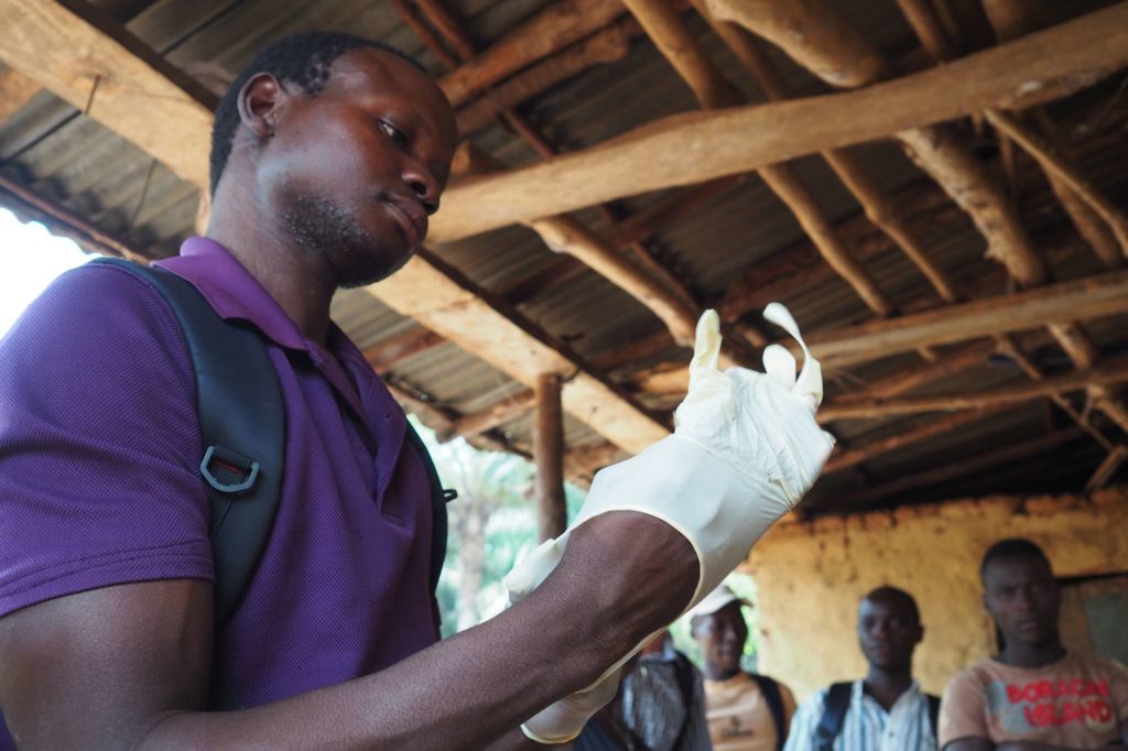 Community Health Worker, Issa, puts on gloves.