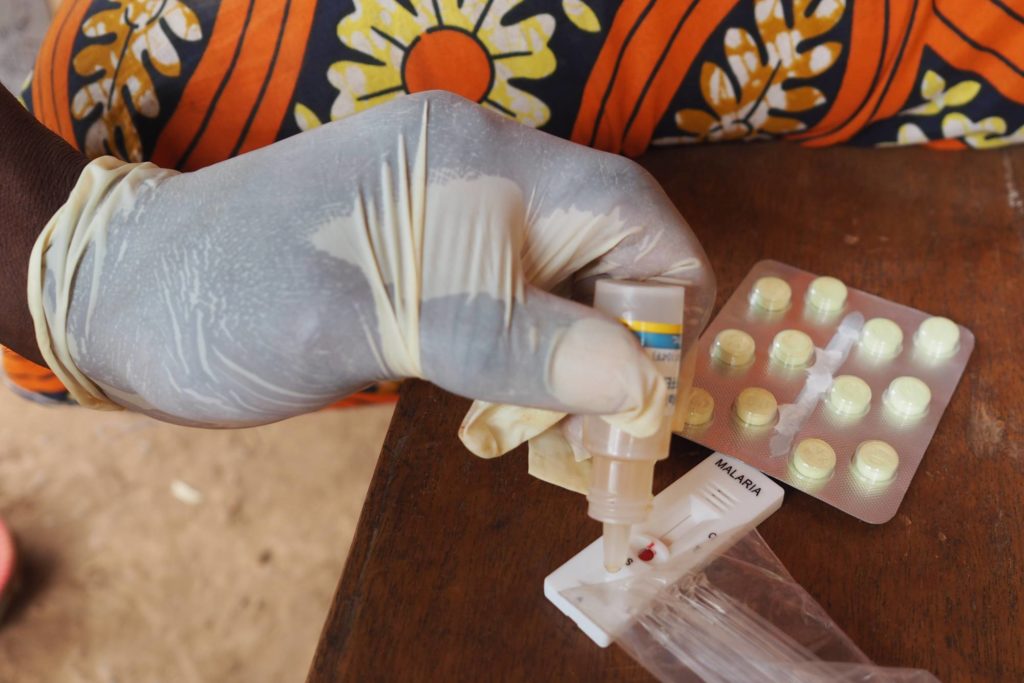 A gloved hand drops malaria testing fluid in to a blood sample.